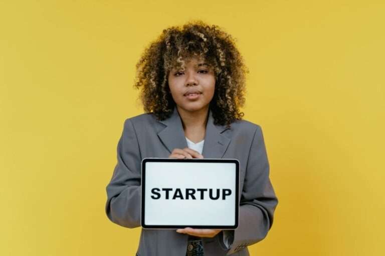 Portrait of a woman holding a tablet showing the word 'STARTUP' against a yellow background.